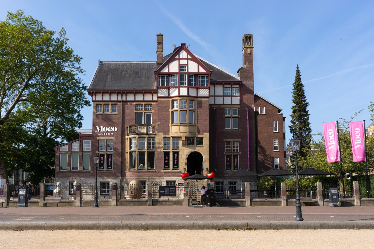Facade of the Moco Museum building with red brick, bay windows, and white decorative timber, under a blue sky.