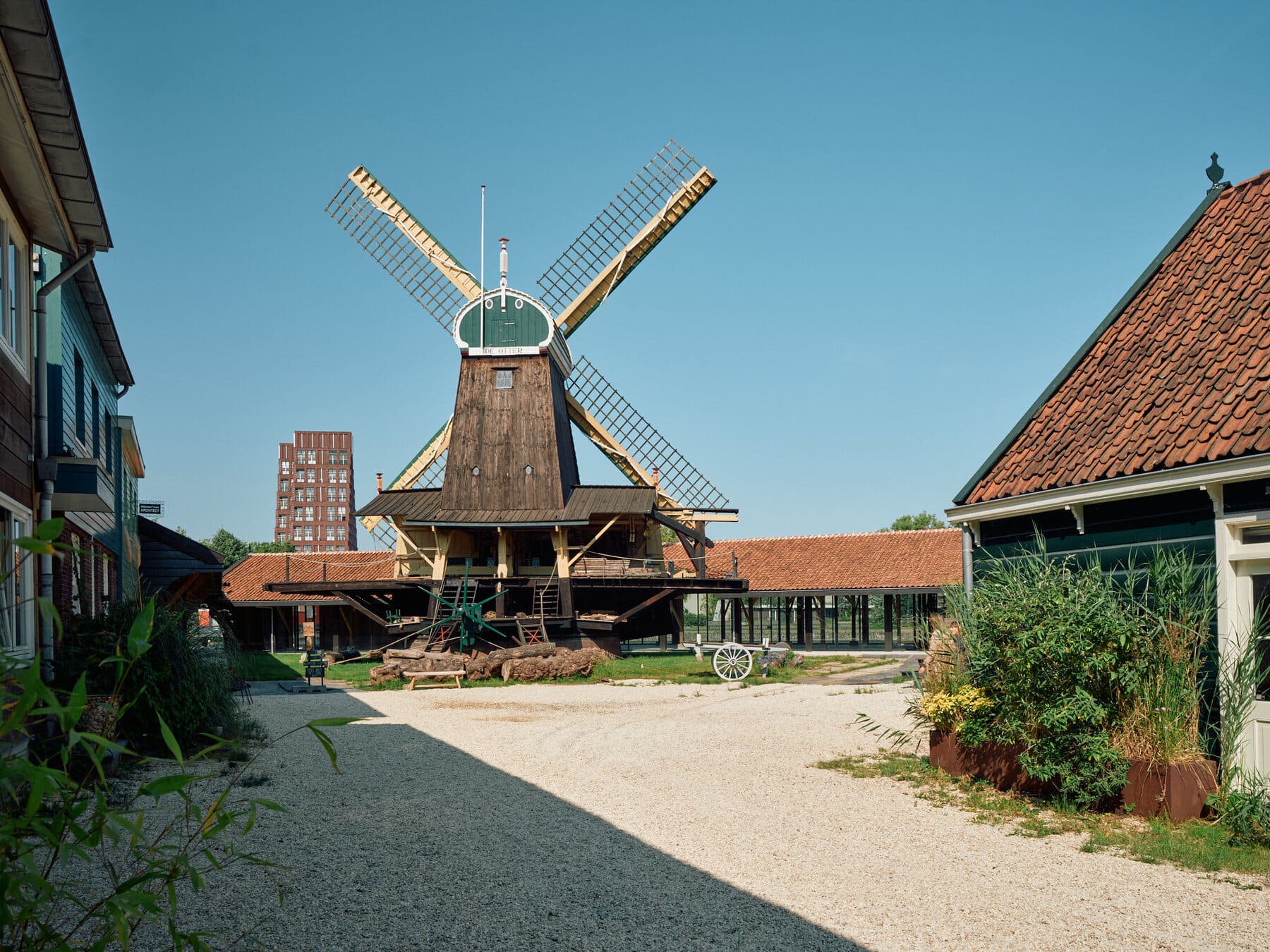 Historic windmill with large wooden sails in a courtyard flanked by timber-framed buildings under a clear blue sky