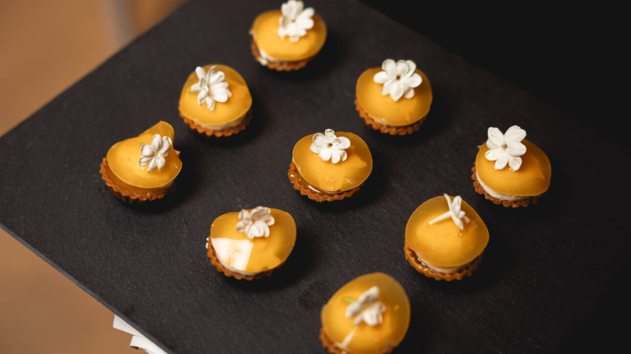 Small cupcakes with bright yellow glaze and white flower decorations arranged on a dark slate tray