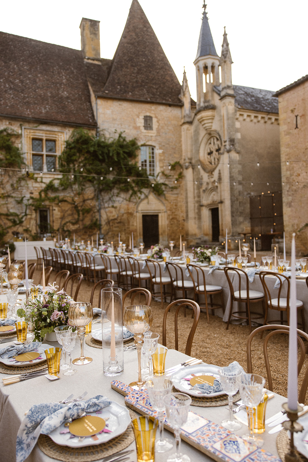 Long banquet tables set for an outdoor wedding in a historic stone courtyard with candles and floral centerpieces.