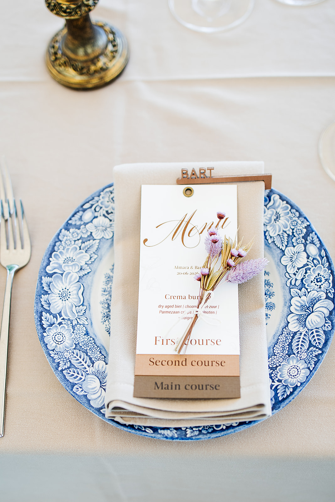 Elegant place setting with a blue floral plate, beige napkin, and a menu card adorned with dried flowers.