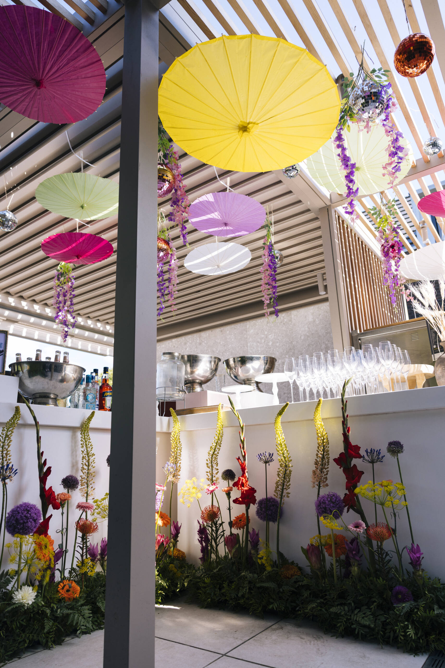 Colorful parasols hanging from the ceiling above a bar, with disco balls and cascading flowers.